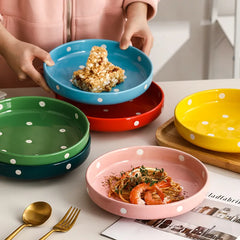 A collection of vibrant polka dot ceramic plates in various colors, including blue, red, yellow, pink, and green, stacked on a table with food and cutlery