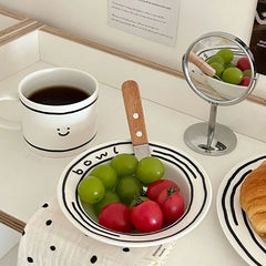 Cheerful ceramic dinnerware set including a plate, bowl, and mug with smiling faces and hand-drawn text on a white background